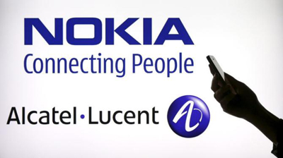 A woman holds a smartphone in front of a screen displaying both Nokia and Alcatel Lucent logos in this photo illustration in Paris, April 14, 2015. REUTERS/Benoit Tessier